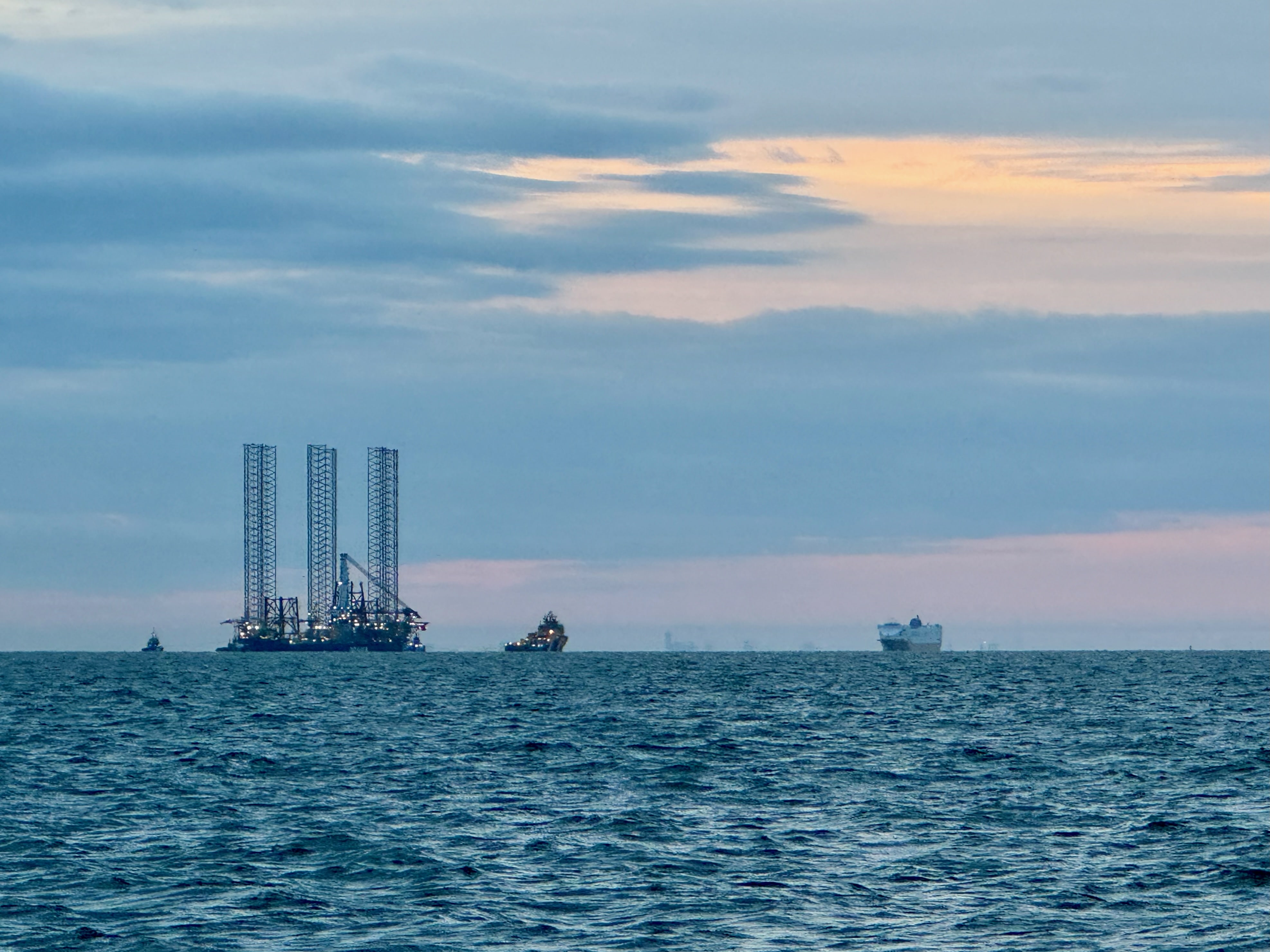 Mehrere Boote ziehen eine Plattform für Windkrafträder durch das Wasser